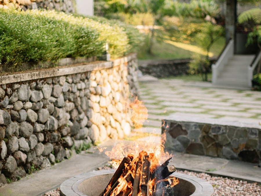 A dry-stacked stone wall beside a paved patio with a lit fire pit