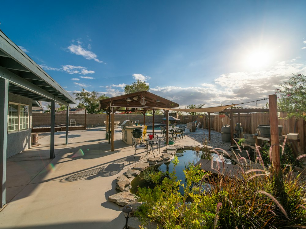 A residential backyard with a covered patio, pool and planted beds